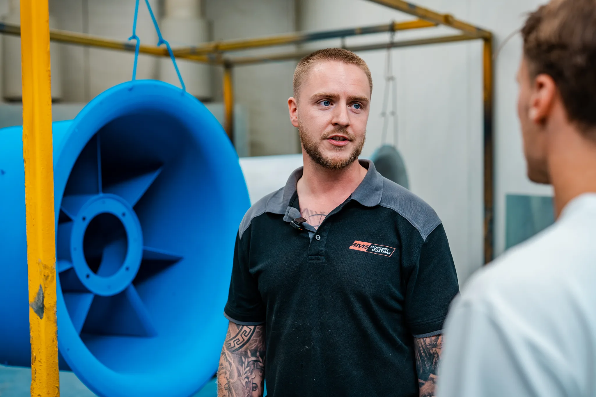 Medewerker van BMS Coating in werkkleding in de productiehal naast blauwe industriële koker