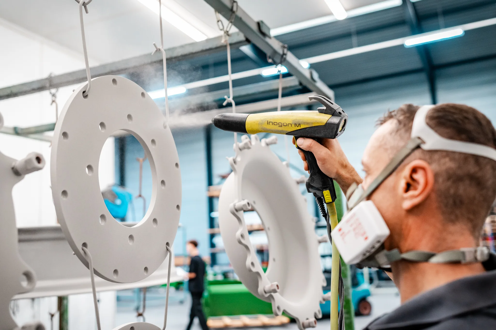 Medewerker poedercoat industriële metalen onderdelen in de spuitcabine van BMS Coating
