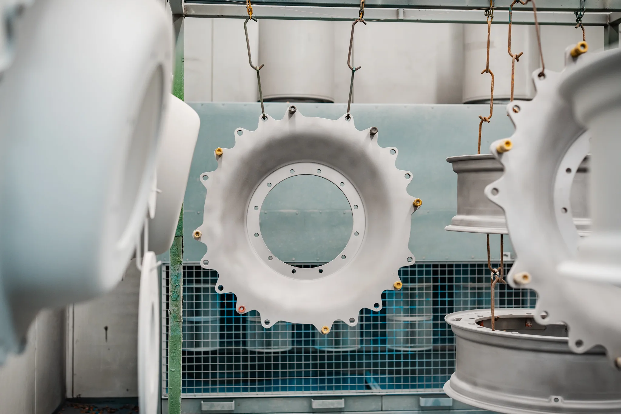 Wit gecoate industriële ronde onderdelen hangen aan een transportrek in de cabine van BMS Coating