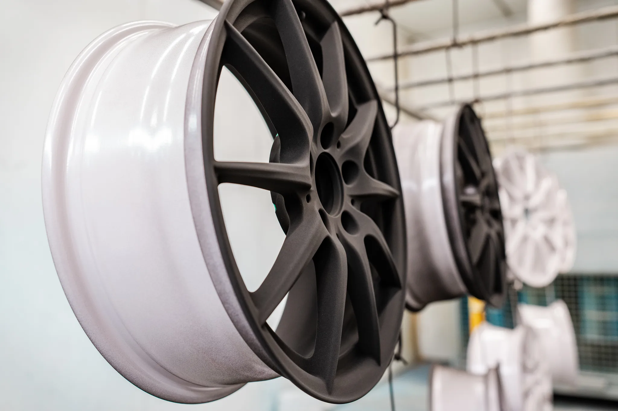 Donkergrijze en witte poedergecoate velgen hangen in de spuitcabine van BMS Coating