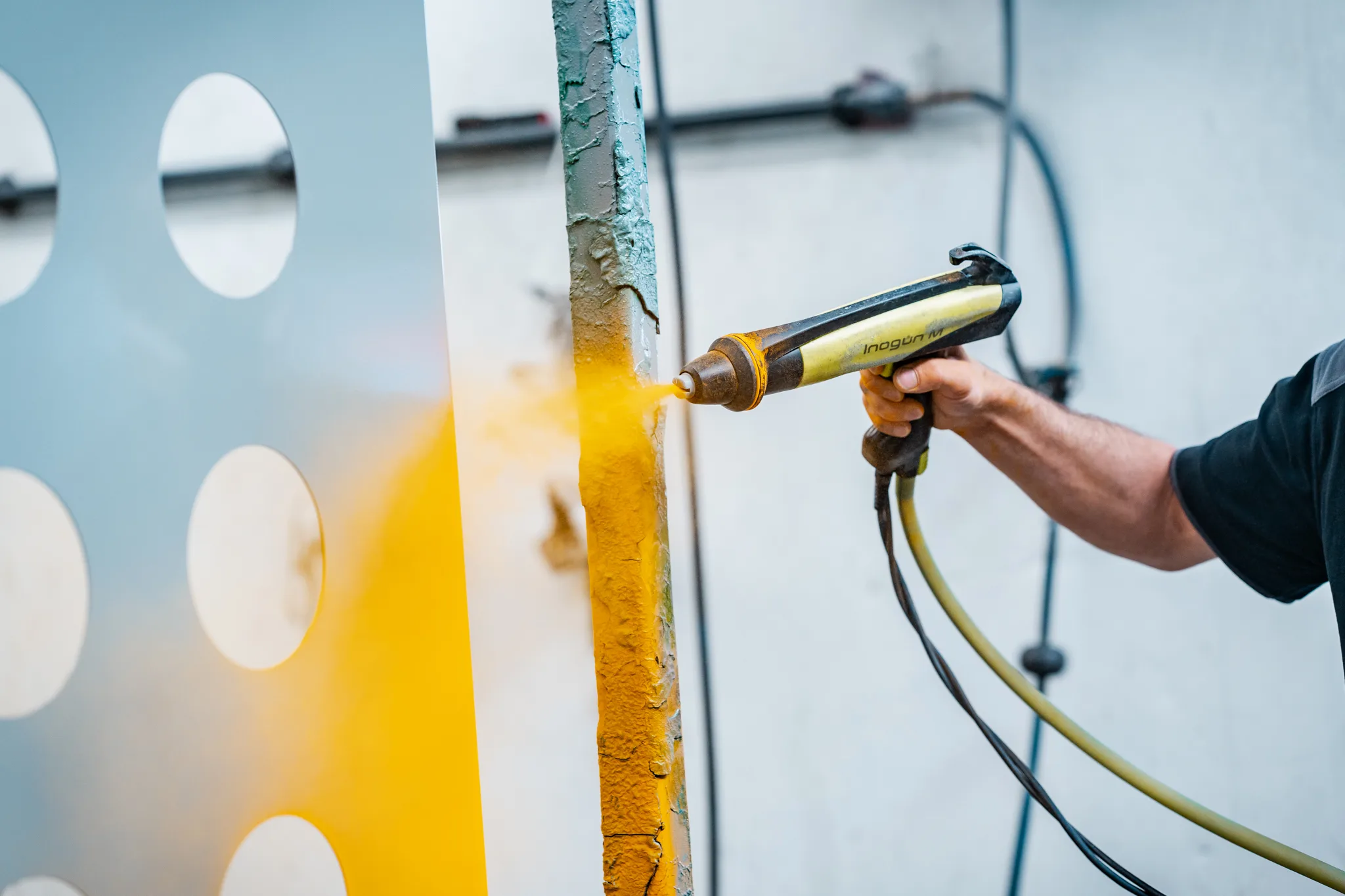 Spuitpistool brengt gele poedercoating aan op een geperforeerde staalplaat bij BMS Coating