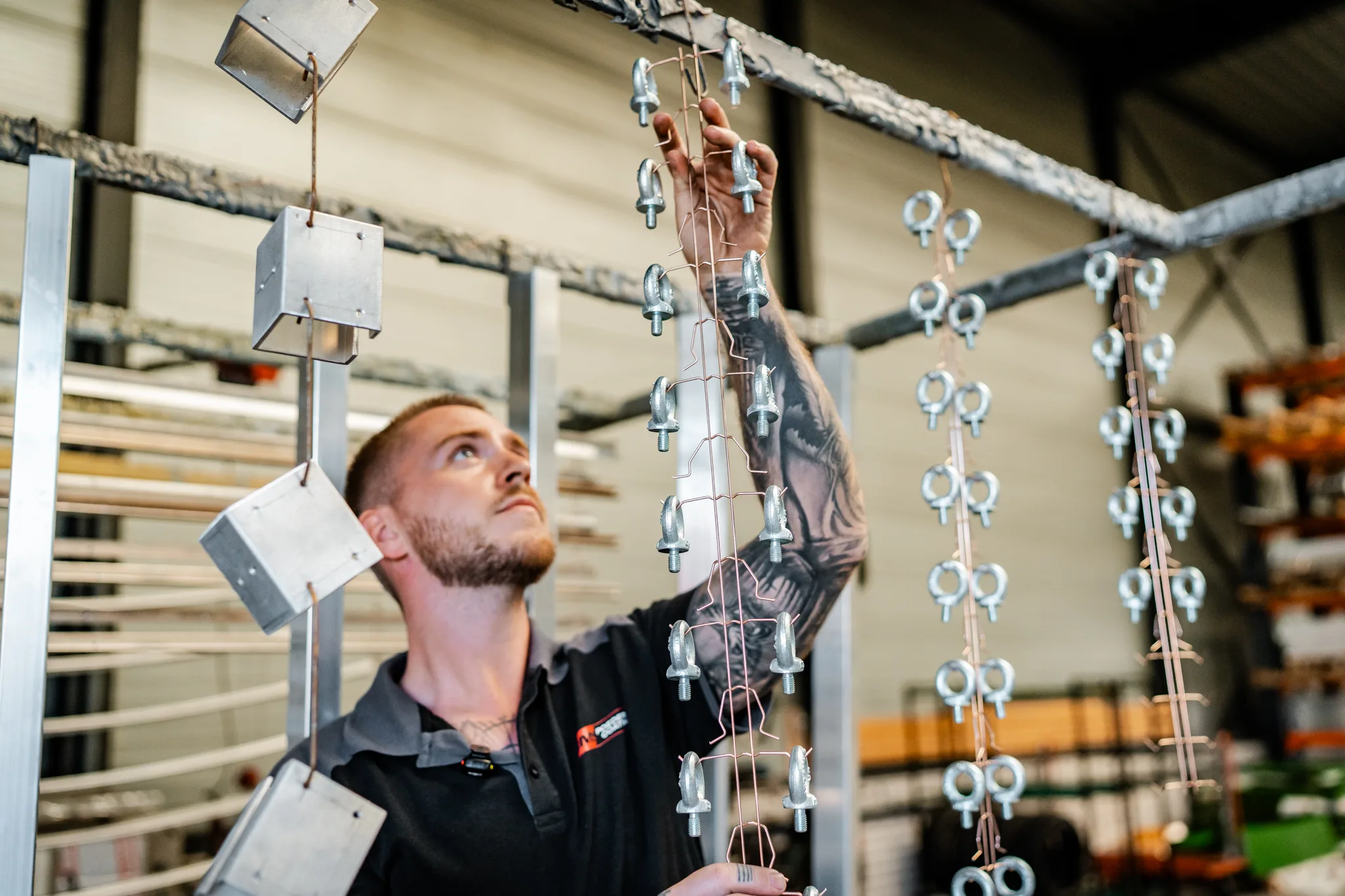 Medewerker bereidt metalen onderdelen voor door ze aan het transportrek te hangen bij BMS Coating