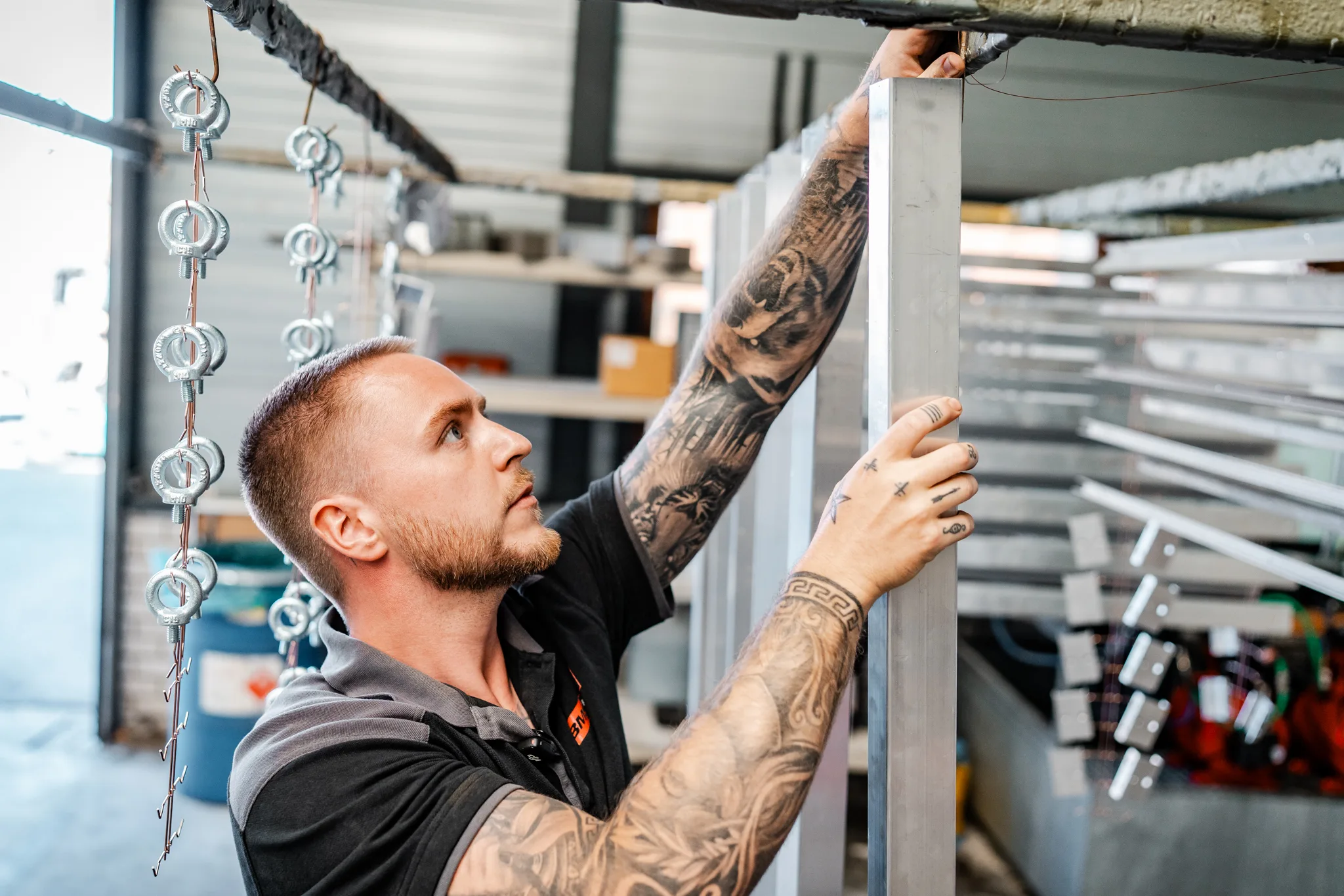 Medewerker van BMS Coating hangt aluminium constructieprofielen aan het transportrek