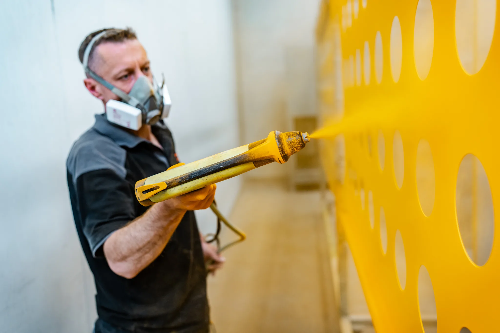 Medewerker van BMS Coating poedercoat een industrieel onderdeel met geel poedercoatpoeder