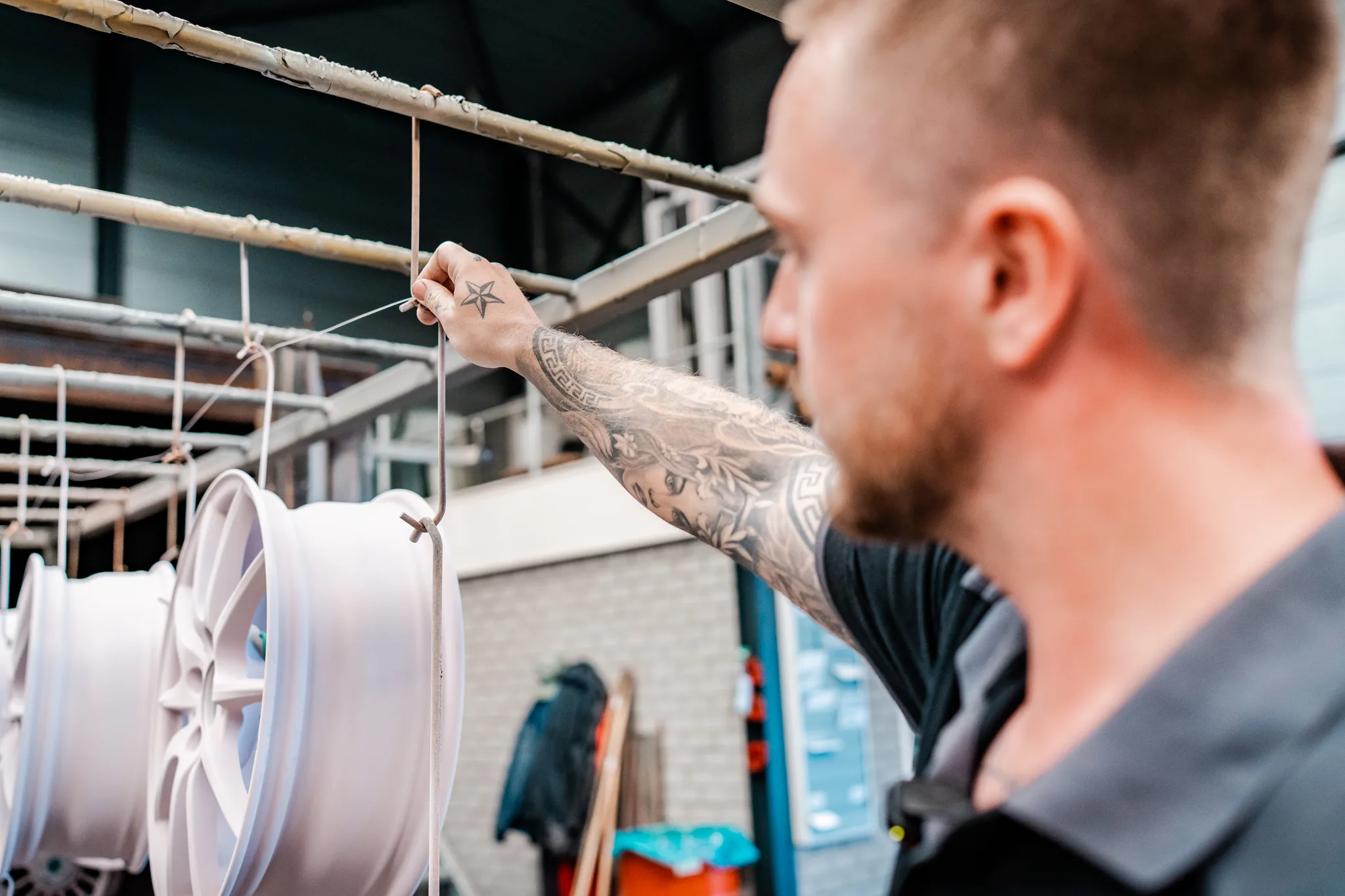Medewerker hangt een witte velg aan het ophangrek bij BMS Coating ter voorbereiding op poedercoaten
