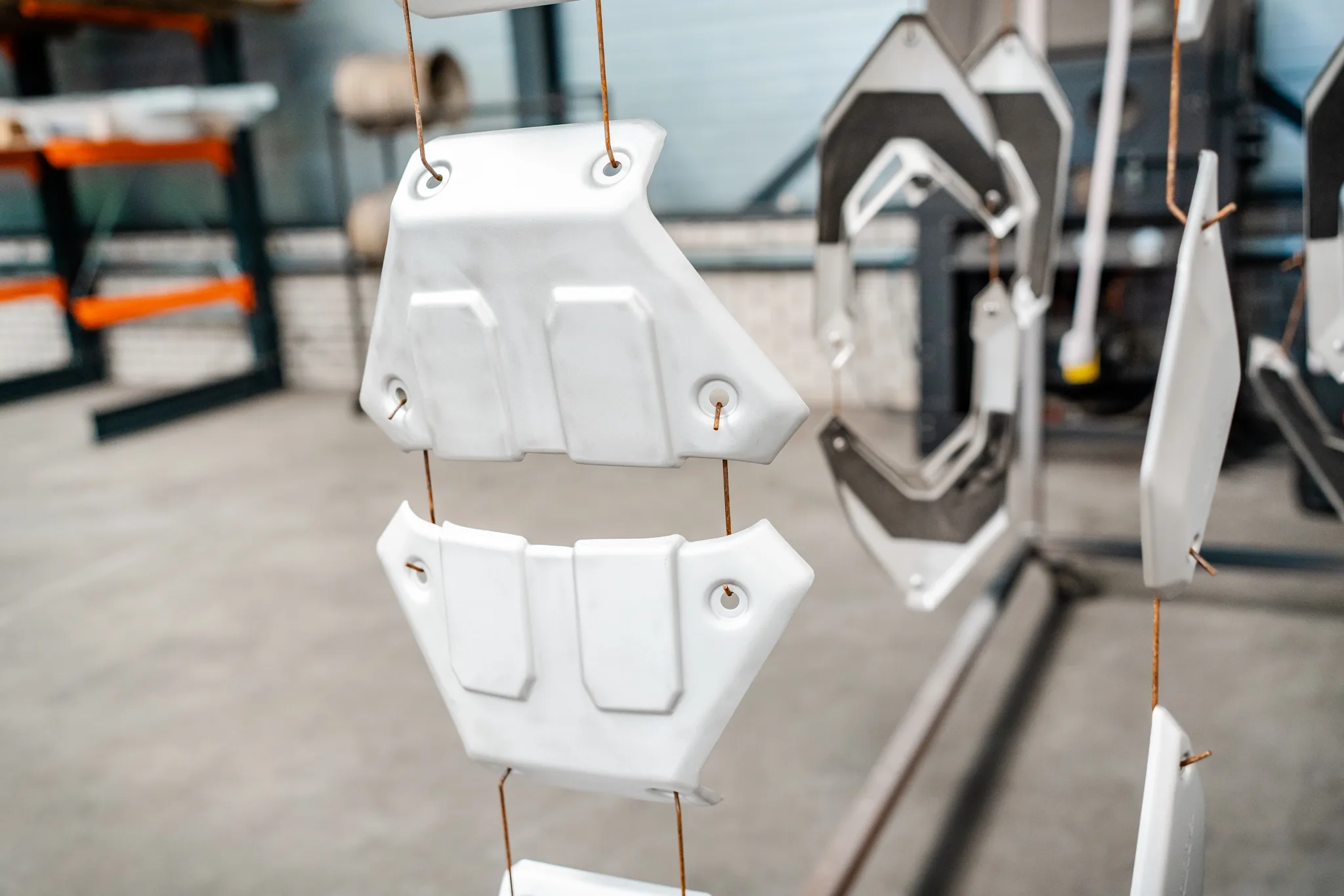 Wit gecoate voertuigonderdelen en bodemplaten hangen aan het transportrek bij BMS Coating