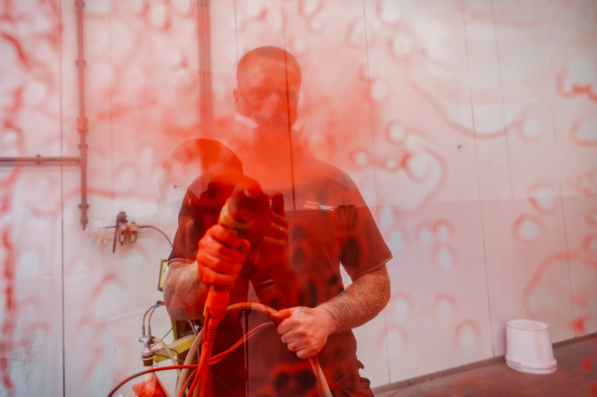 Medewerker omgeven door rood poedercoatpoeder in de spuitcabine van BMS Coating