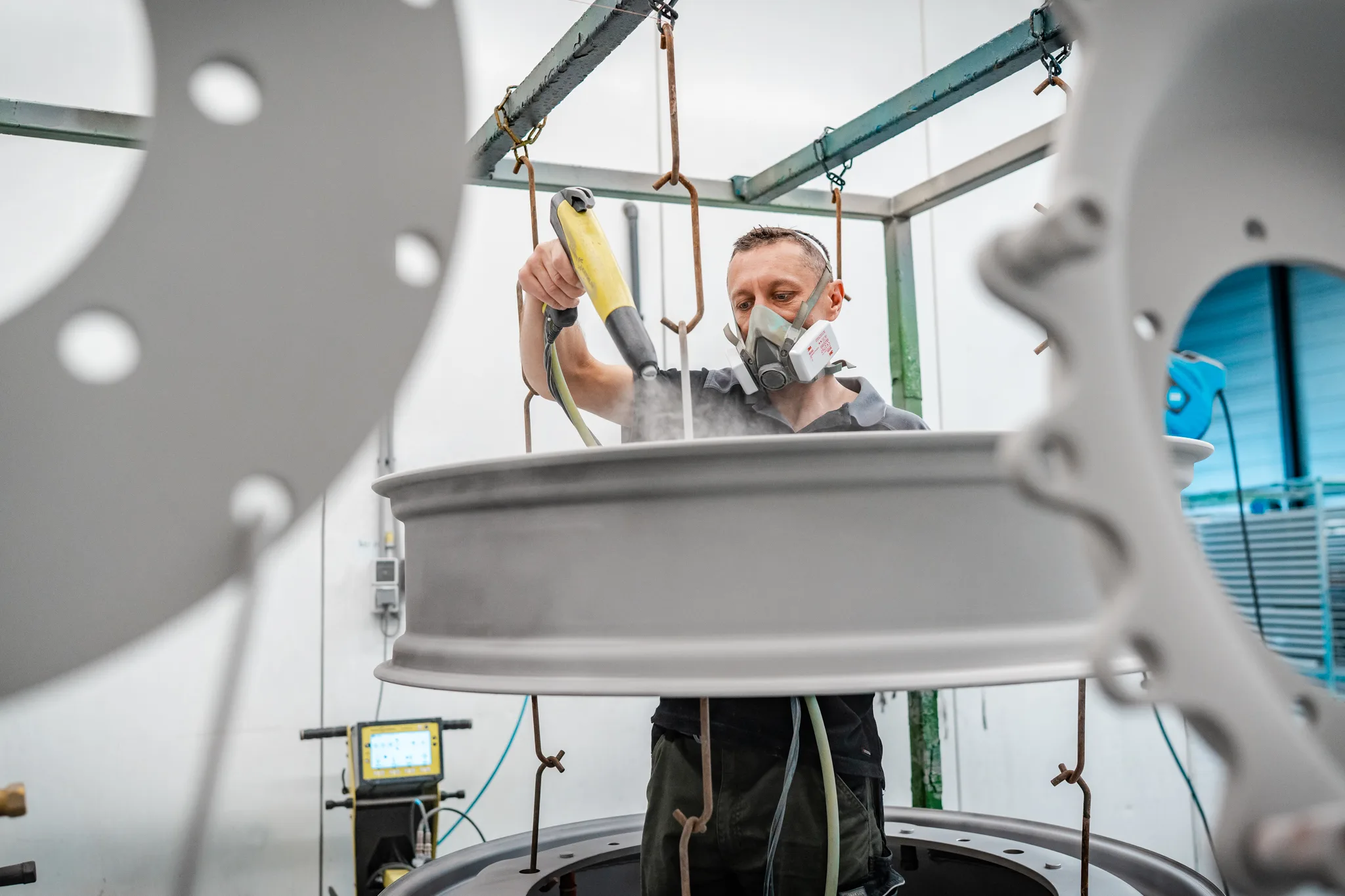 Close-up van medewerker die een velg poedercoat in de spuitcabine van BMS Coating