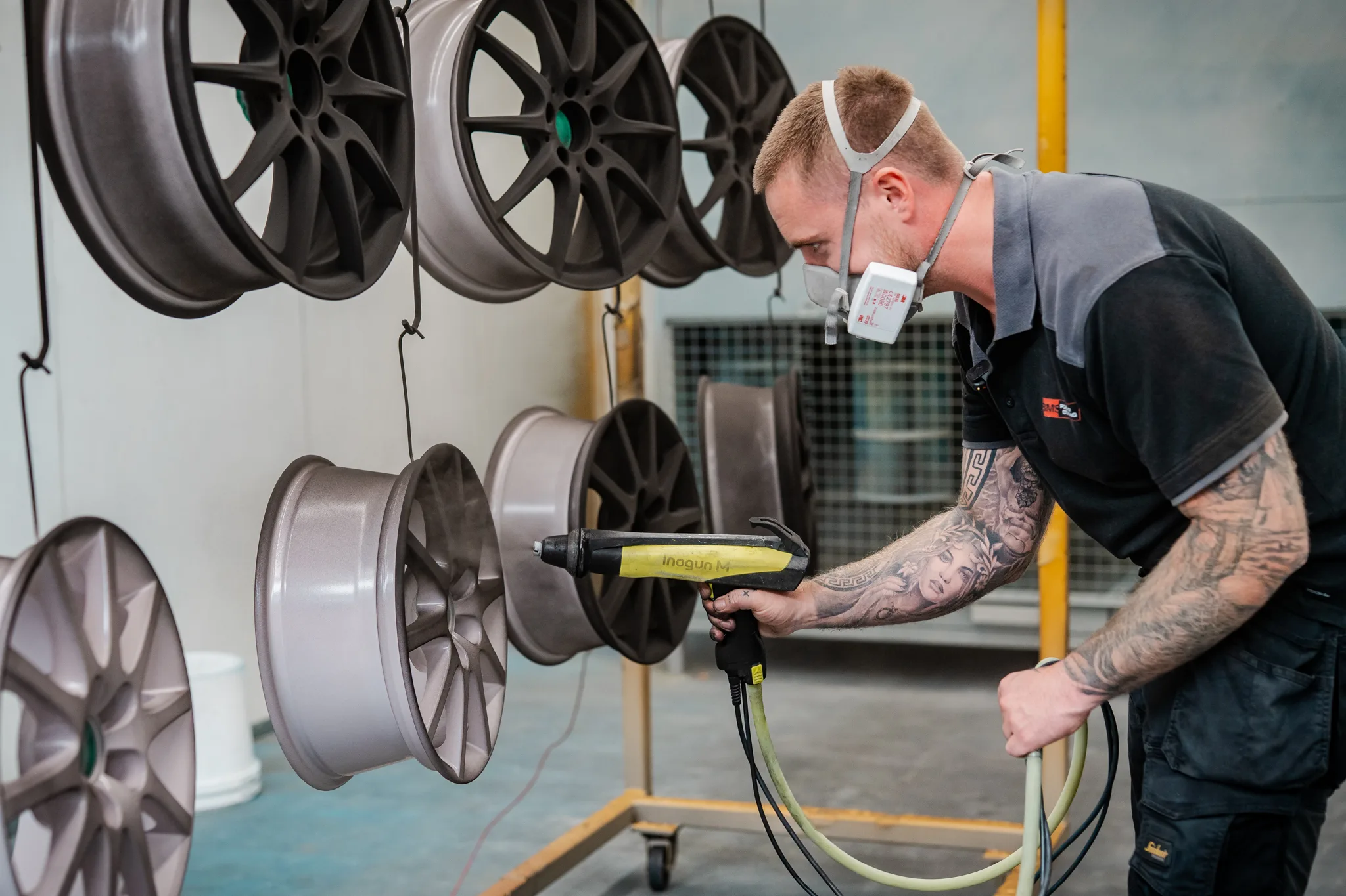 Medewerker van BMS Coating met spuitpistool poedercoat een rij velgen in de cabine
